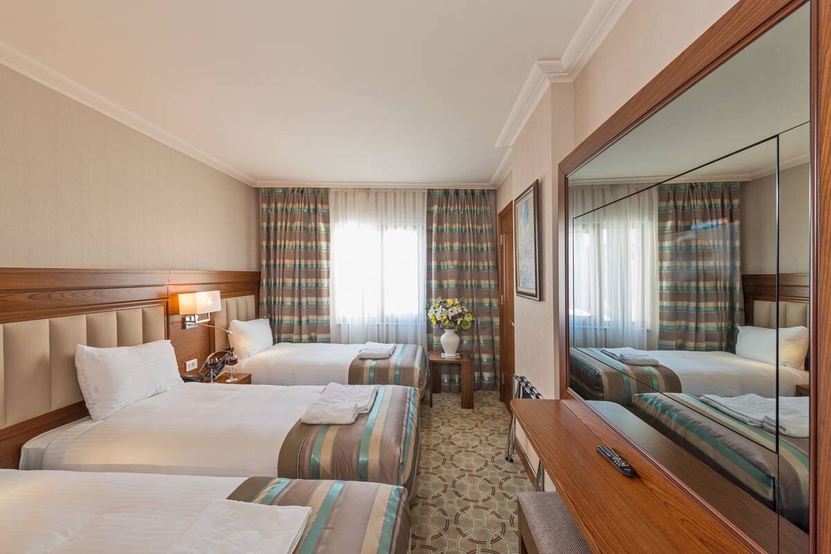 A hotel room with two beds, a desk, a mirror, and a window with curtains.