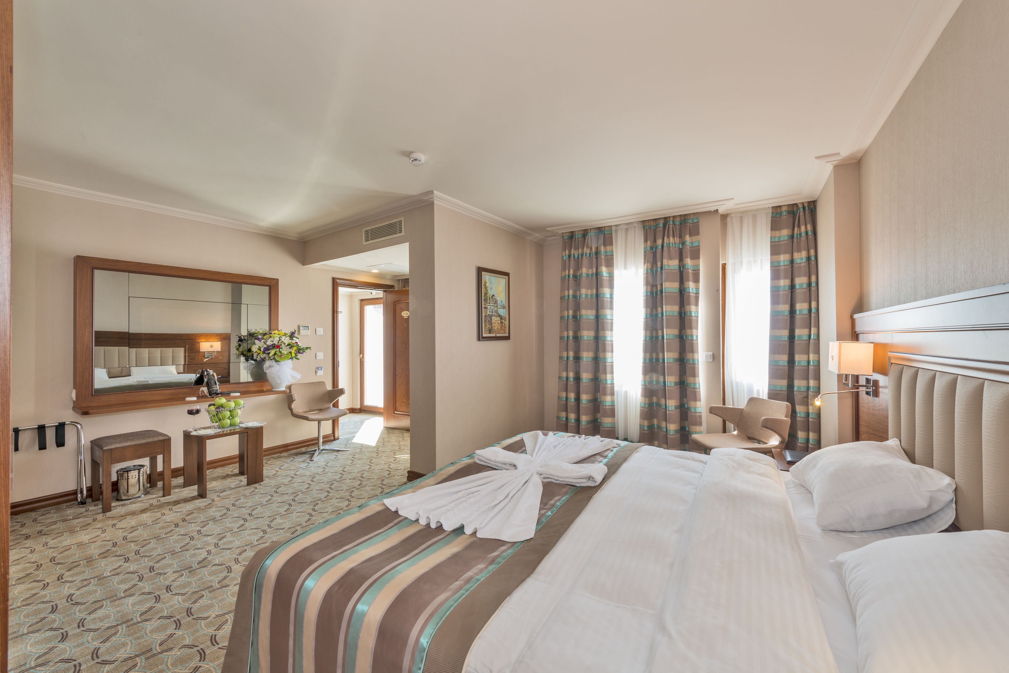 A hotel room with a large bed, a sitting area with a chair, a small table with a vase of flowers, and a large mirror.