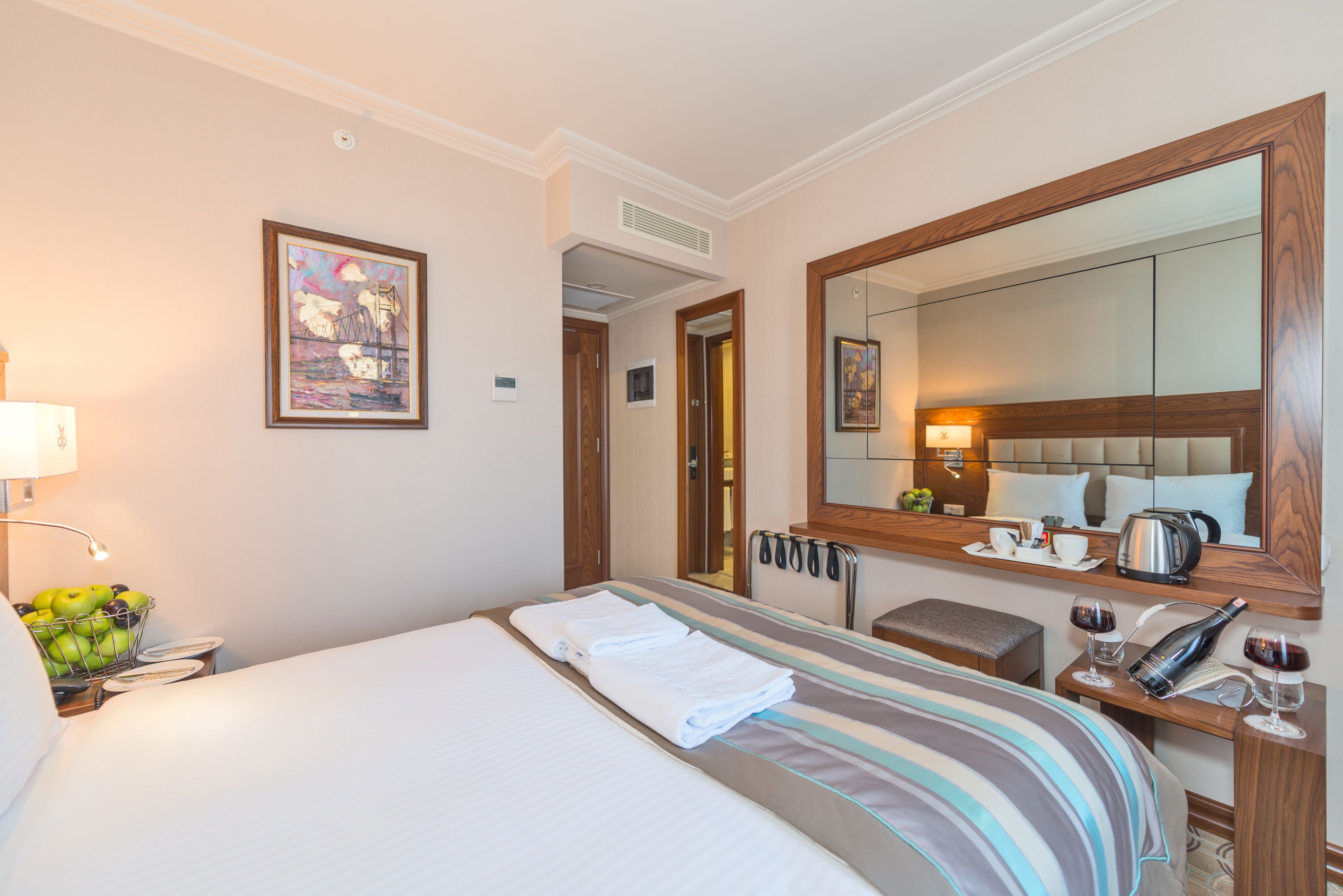 Una habitación de hotel con una cama, una mesita de noche con lámpara, un espejo y un cuadro en la pared.