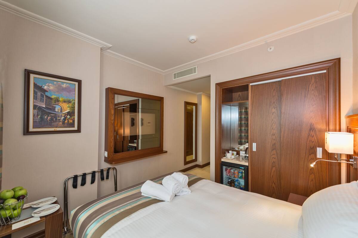 A hotel room with a bed, a bedside table with a lamp, a mirror, and a painting on the wall.