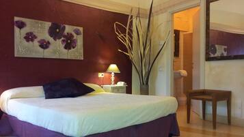 A bedroom with a bed, a nightstand, a lamp, a vase with tall plants, and a chair.