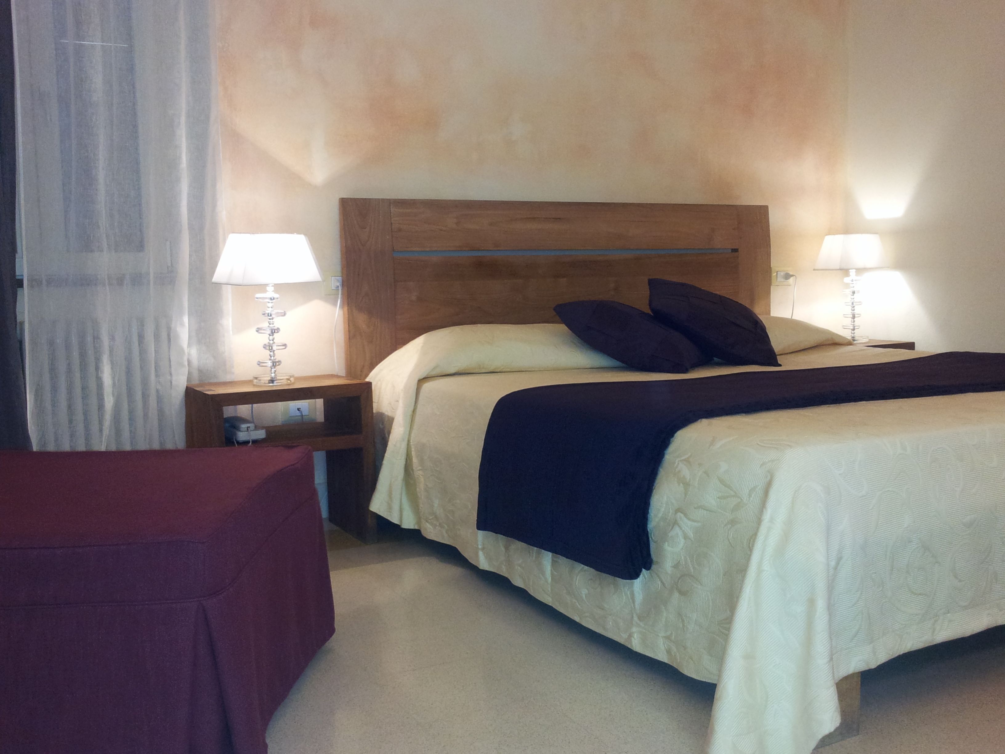 Une chambre d’hôtel avec un lit, deux lampes de chevet, une tête de lit en bois et une chaise rouge.