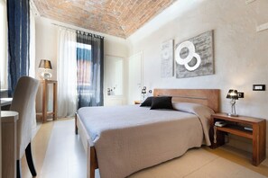 A modern bedroom with a large bed, a wooden nightstand, a desk with a lamp, and a chair. - Hotel Relais al Convento (Vezzano Ligure)