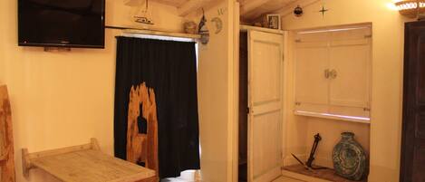 Una habitación con una mesa de madera, un televisor en la pared, un armario y una estantería con un jarrón.