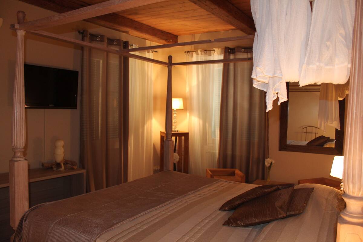 A bedroom with a four-poster bed, a television on the wall, and a mirror.