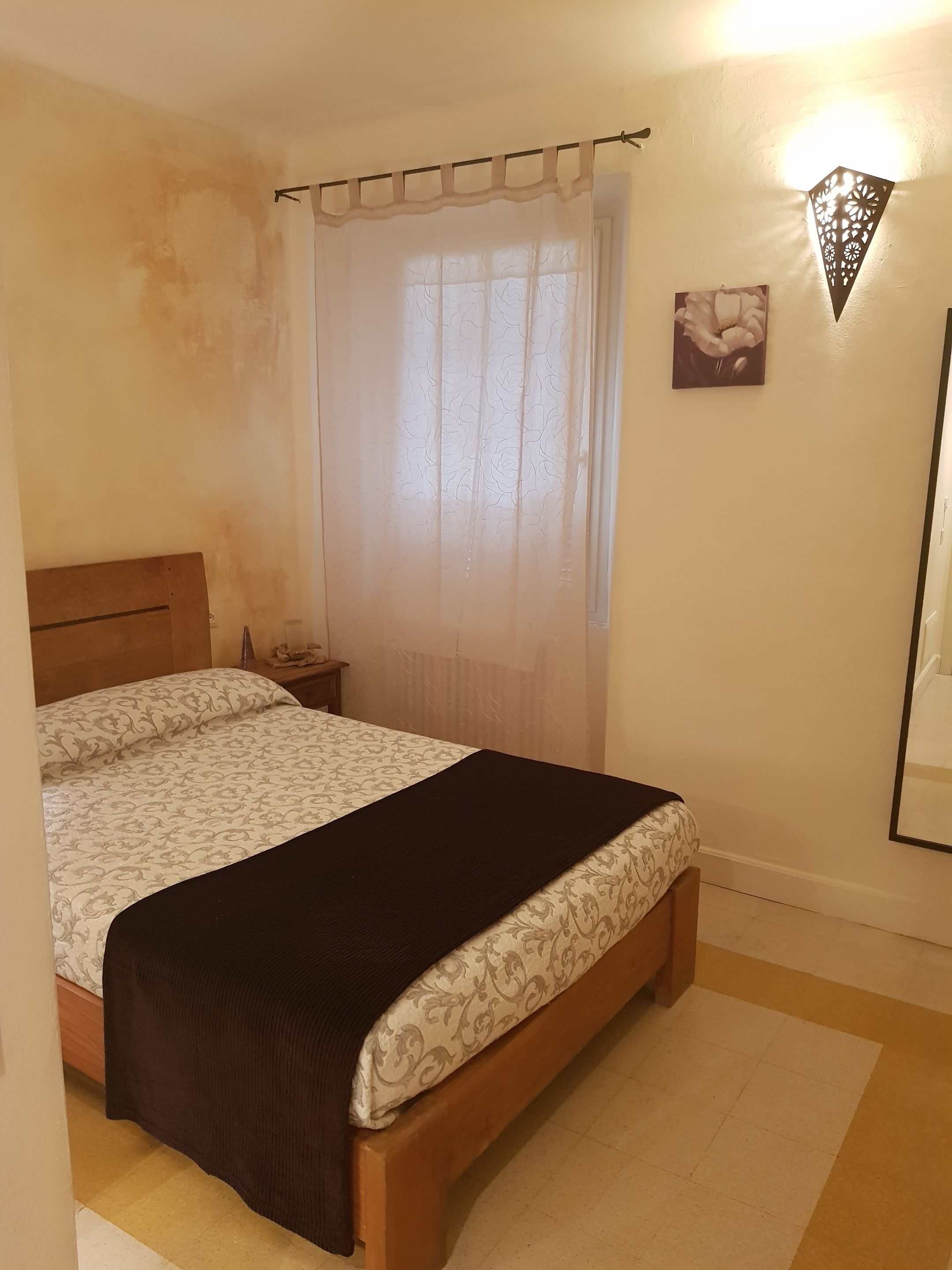 Una camera da letto con un letto, un comodino, una lampada a parete e un quadro appeso al muro.