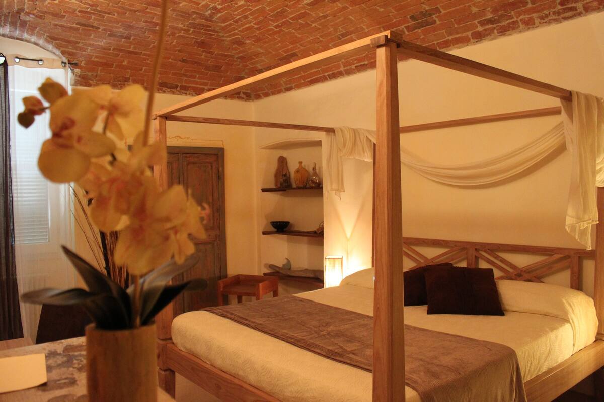 A four-poster bed with a wooden frame, a bedside table, and a vase with flowers.