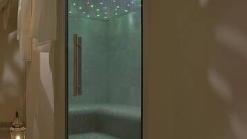 Un spa con paredes de vidrio, suelo de baldosas, banca de madera e iluminación de colores en el techo.