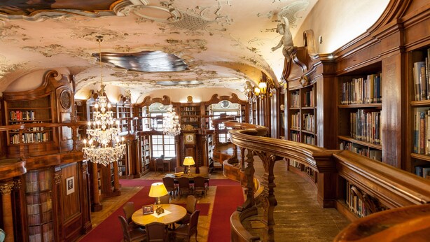 A grand library with ornate woodwork, a red carpet, and a chandelier. - Schloss Leopoldskron (Salzburg)
