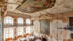 A grand room with ornate ceiling frescoes, large windows, and a checkered floor. - Schloss Leopoldskron (Salzburg)
