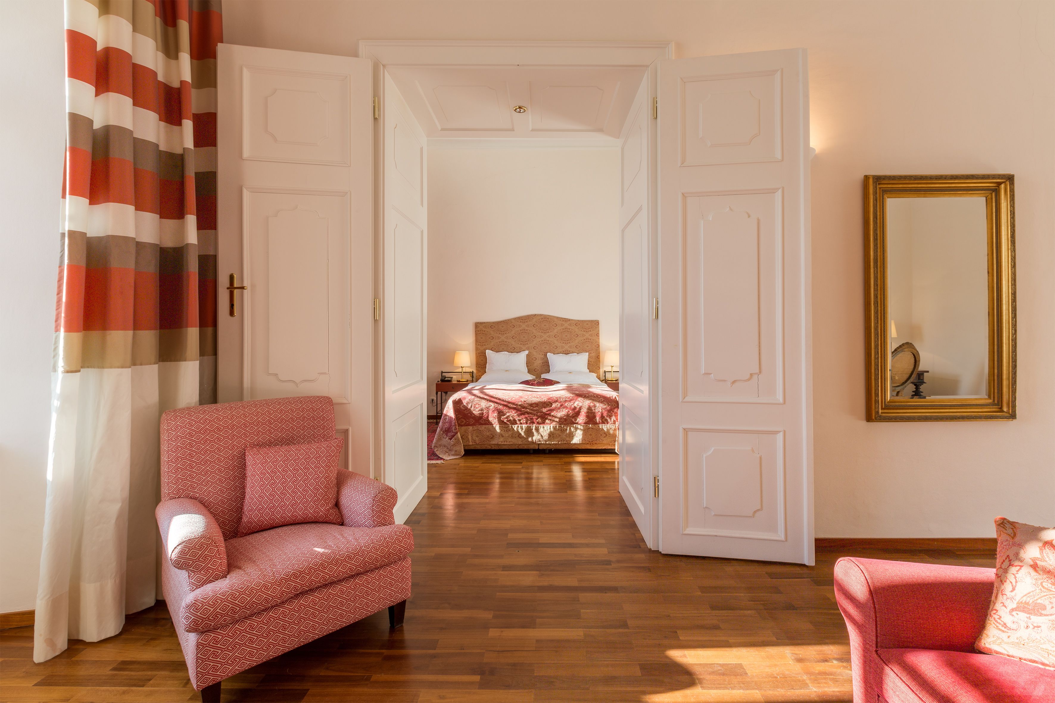Una habitación con una cama, dos sillones, un espejo y una cortina a rayas.