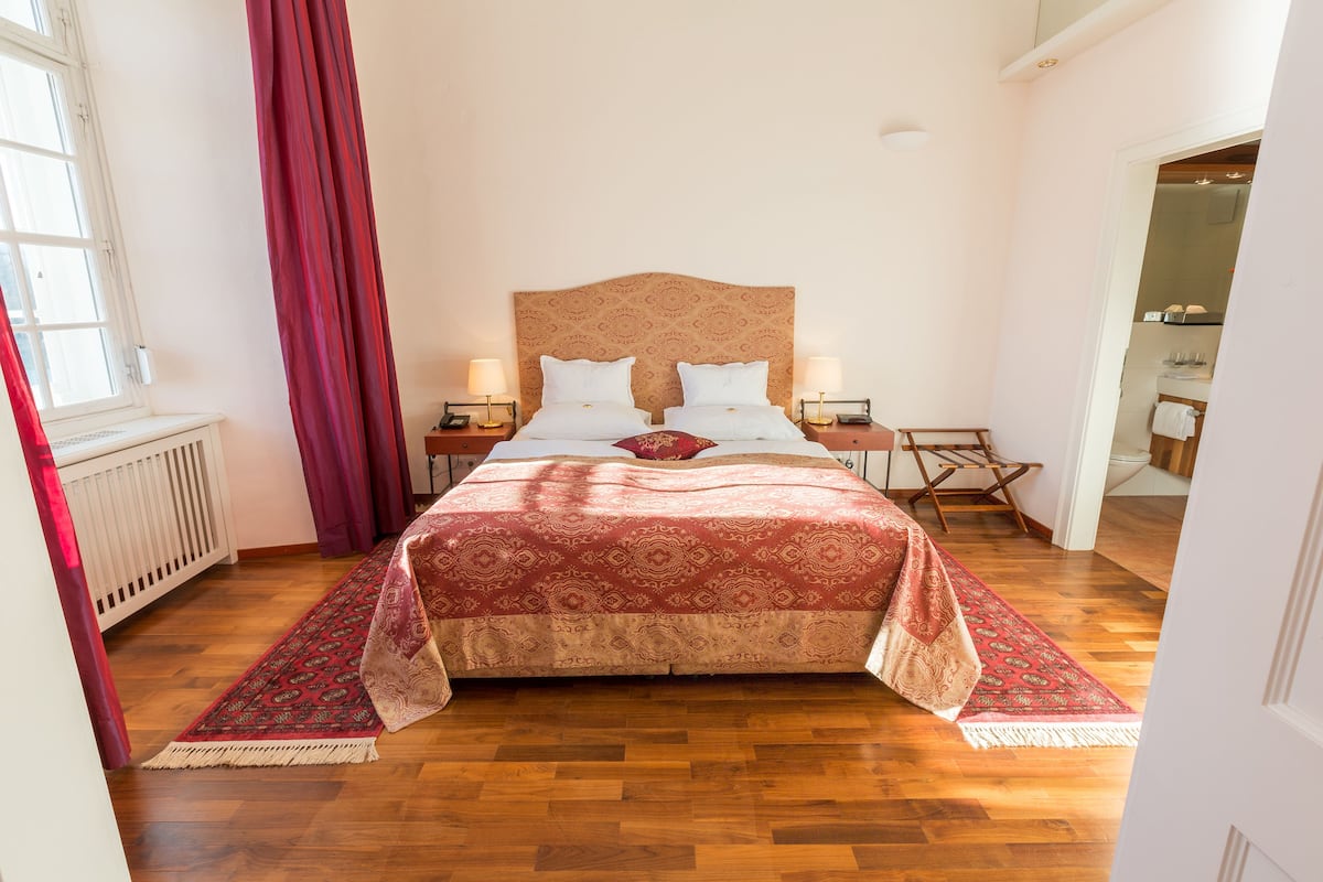 Um quarto bem arrumado com uma cama grande, duas mesas de cabeceira e um cobreleite com padrão vermelho e bege.