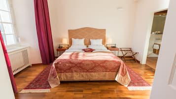 Une chambre à coucher bien rangée, avec un grand lit, deux tables de chevet et une couvre-lit aux motifs rouges et beige.