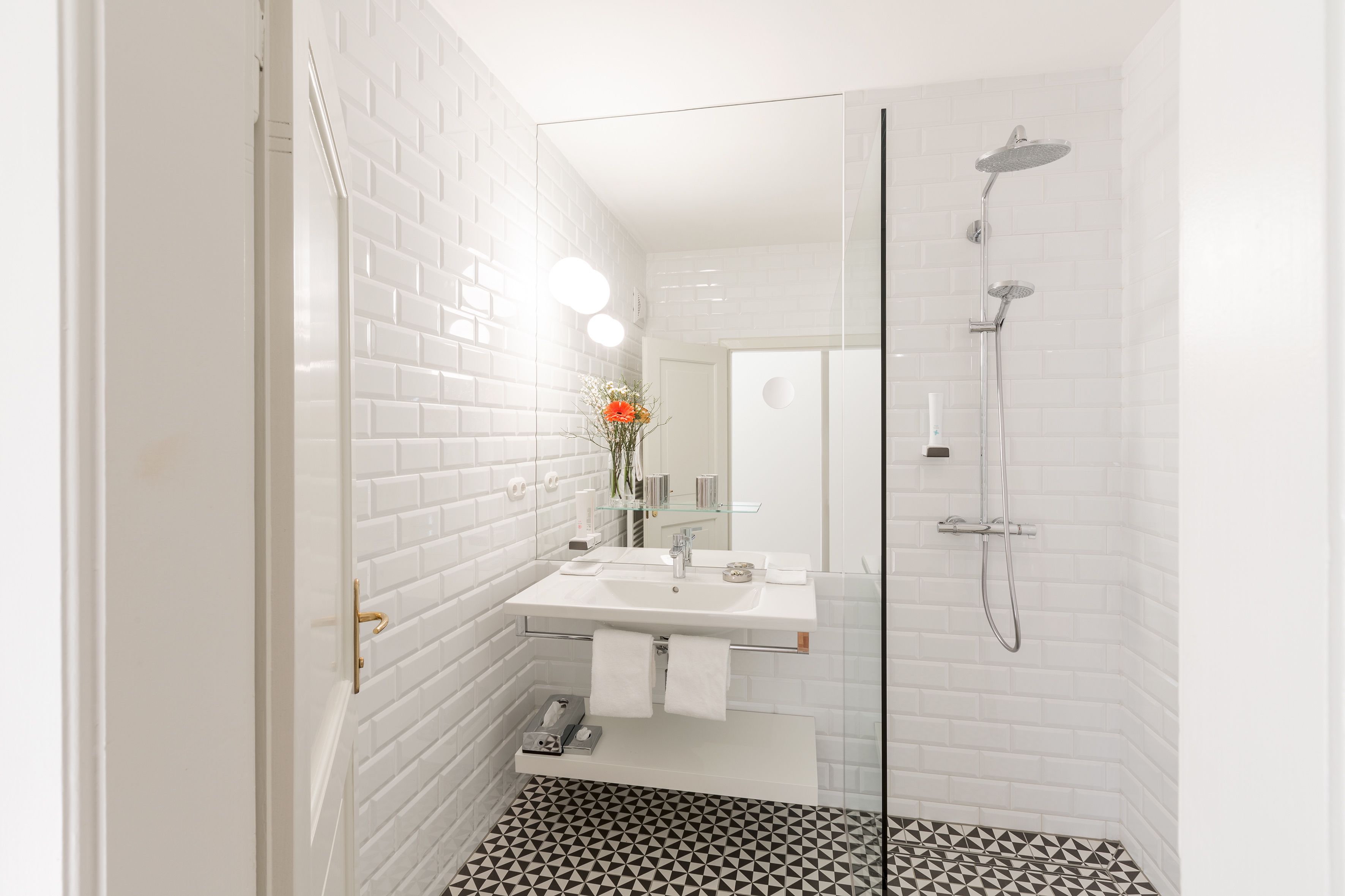 Un baño moderno con azulejos blancos tipo metro, una cabina de ducha de vidrio y un suelo con estampado blanco y negro.