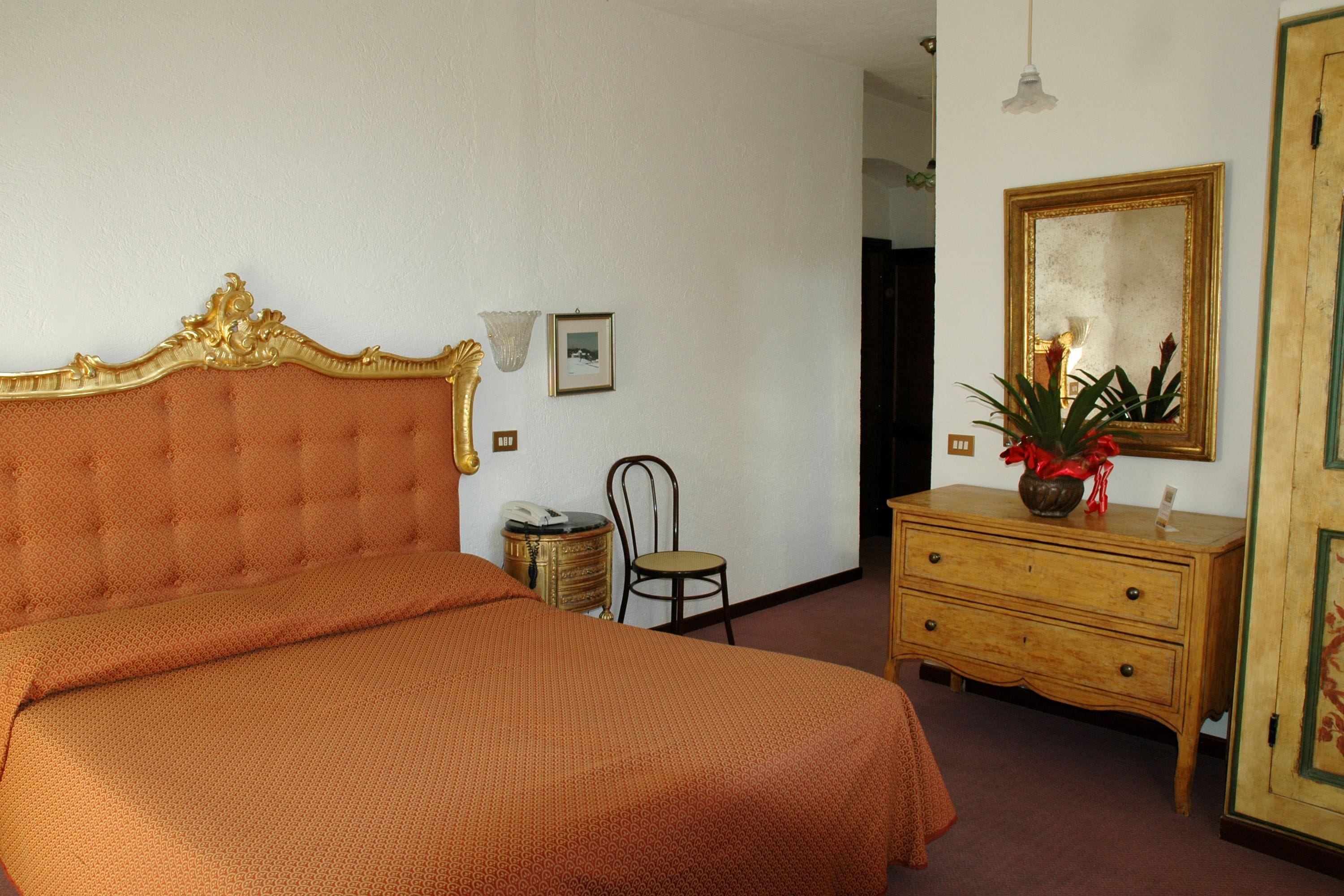 A bedroom with a large bed, a wooden dresser, a chair, and a mirror on the wall.
