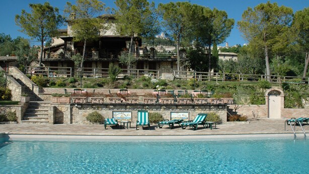Un área de piscina con sillones de descanso y una escalera de piedra que lleva a un edificio con vistas a una colina.