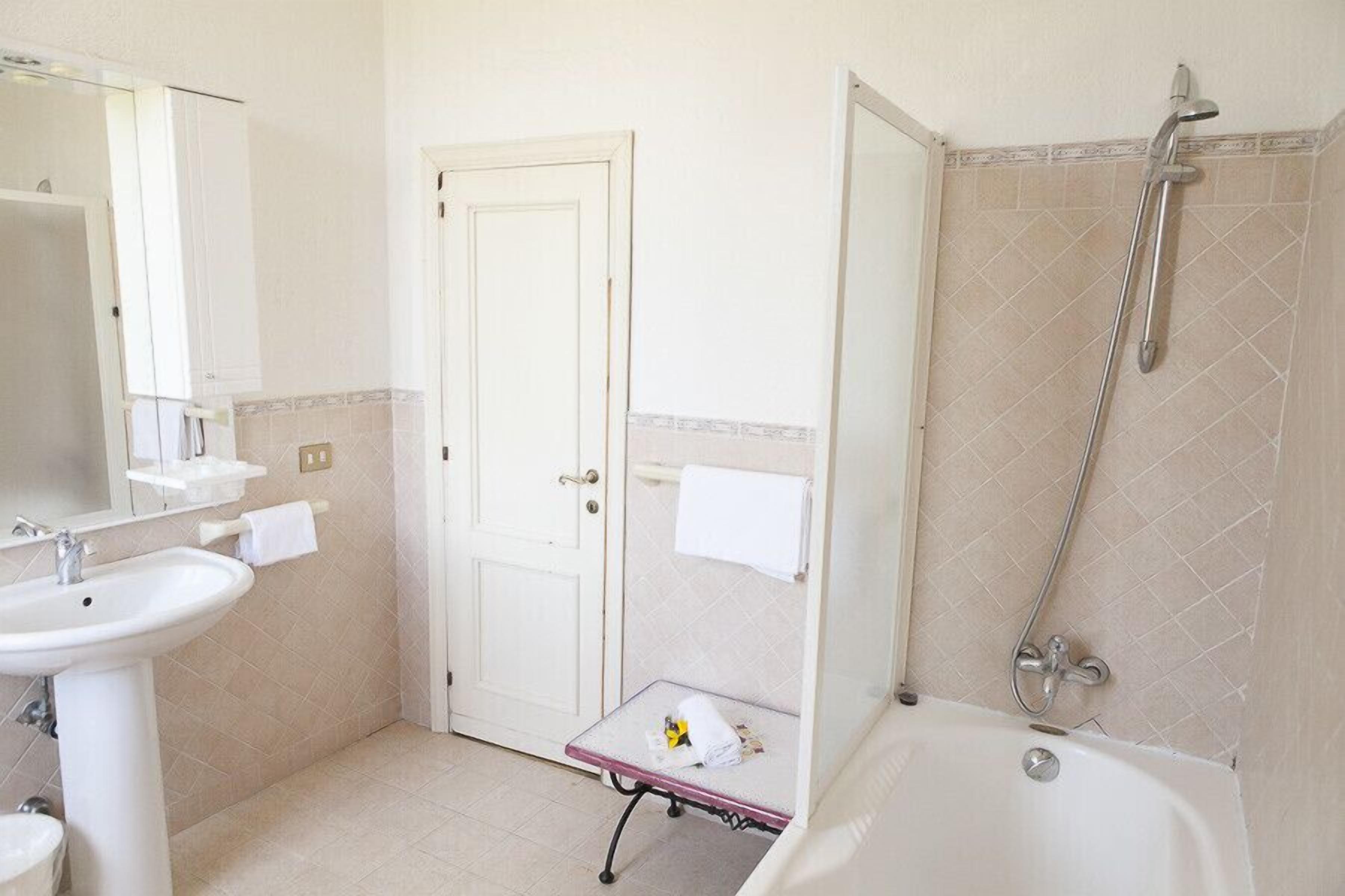 Un bany amb un lavabo, una porta, una dutxa i una taula petita amb una tovallola.
