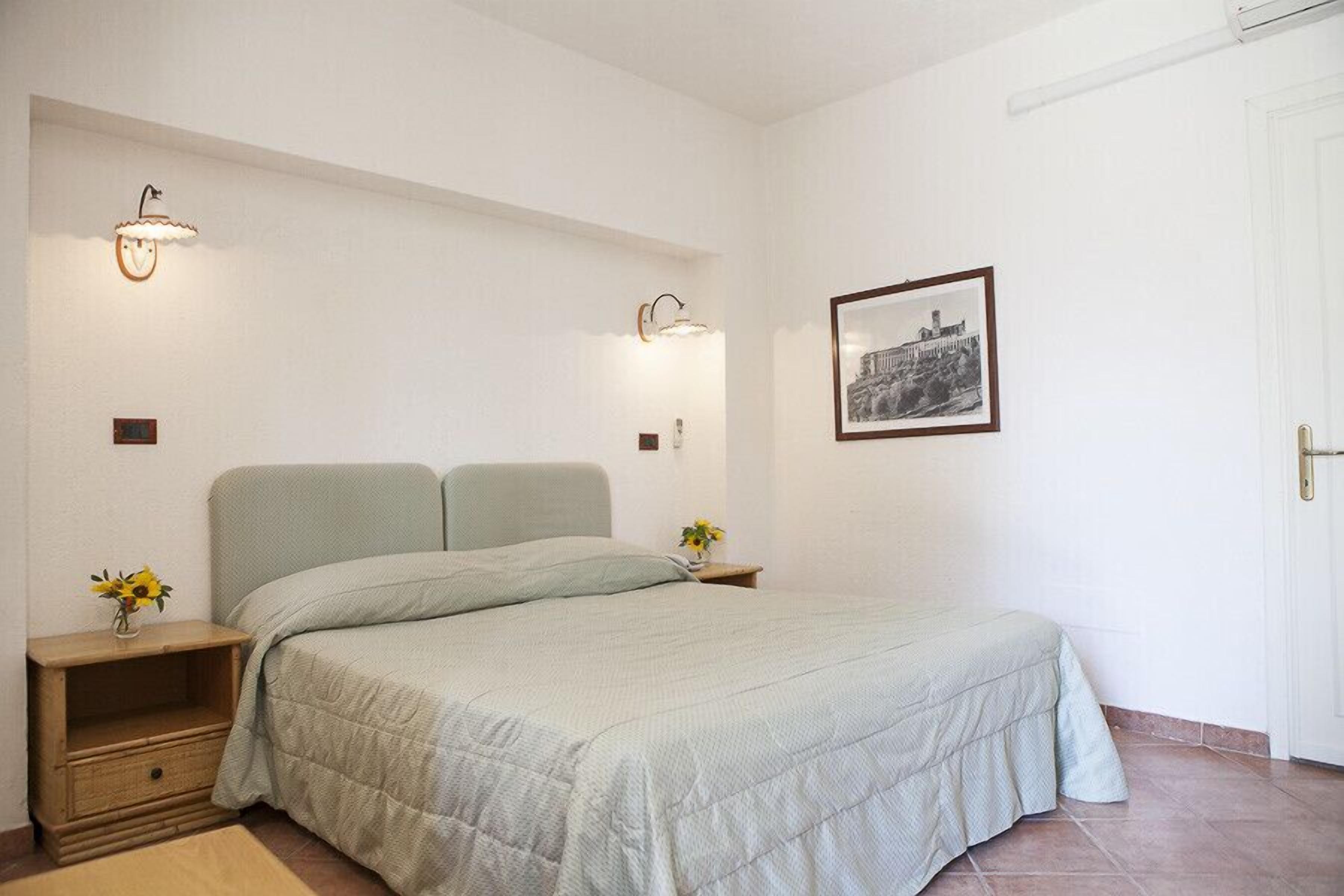 Ein Schlafzimmer mit einem Bett, Nachttischen, Wandleuchten und einem gerahmten Bild an der Wand.