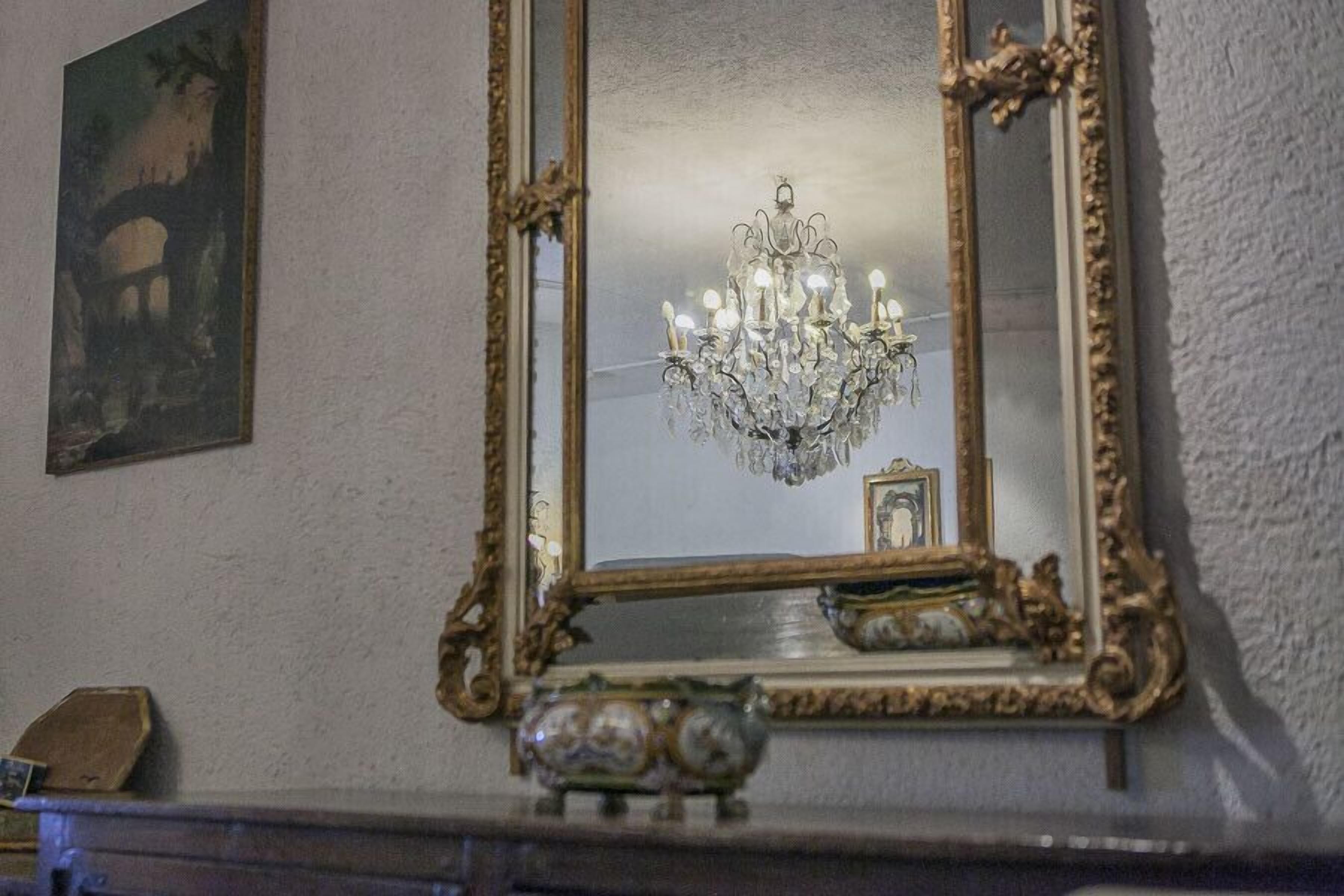 A mirror with an ornate frame, a chandelier, and a small piggy bank on a mantelpiece.