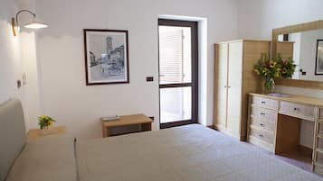 A bedroom with a bed, bedside table, lamp, framed picture, wardrobe, and a window with blinds.