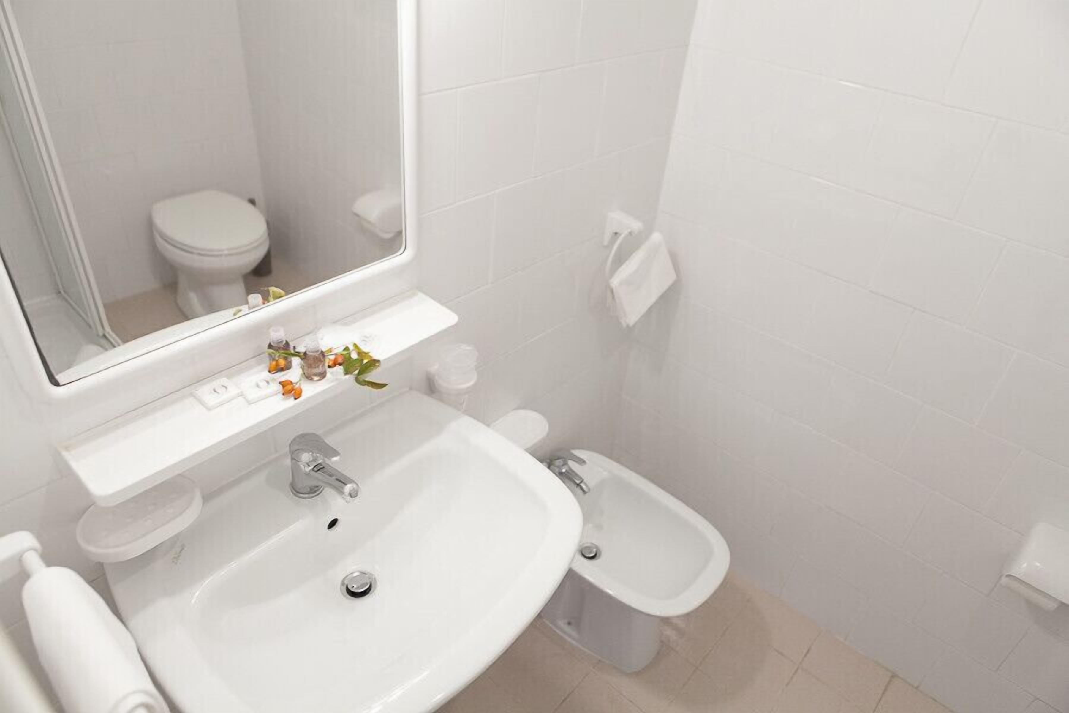 Un bagno moderno con lavandino bianco, specchio, water e bidet.