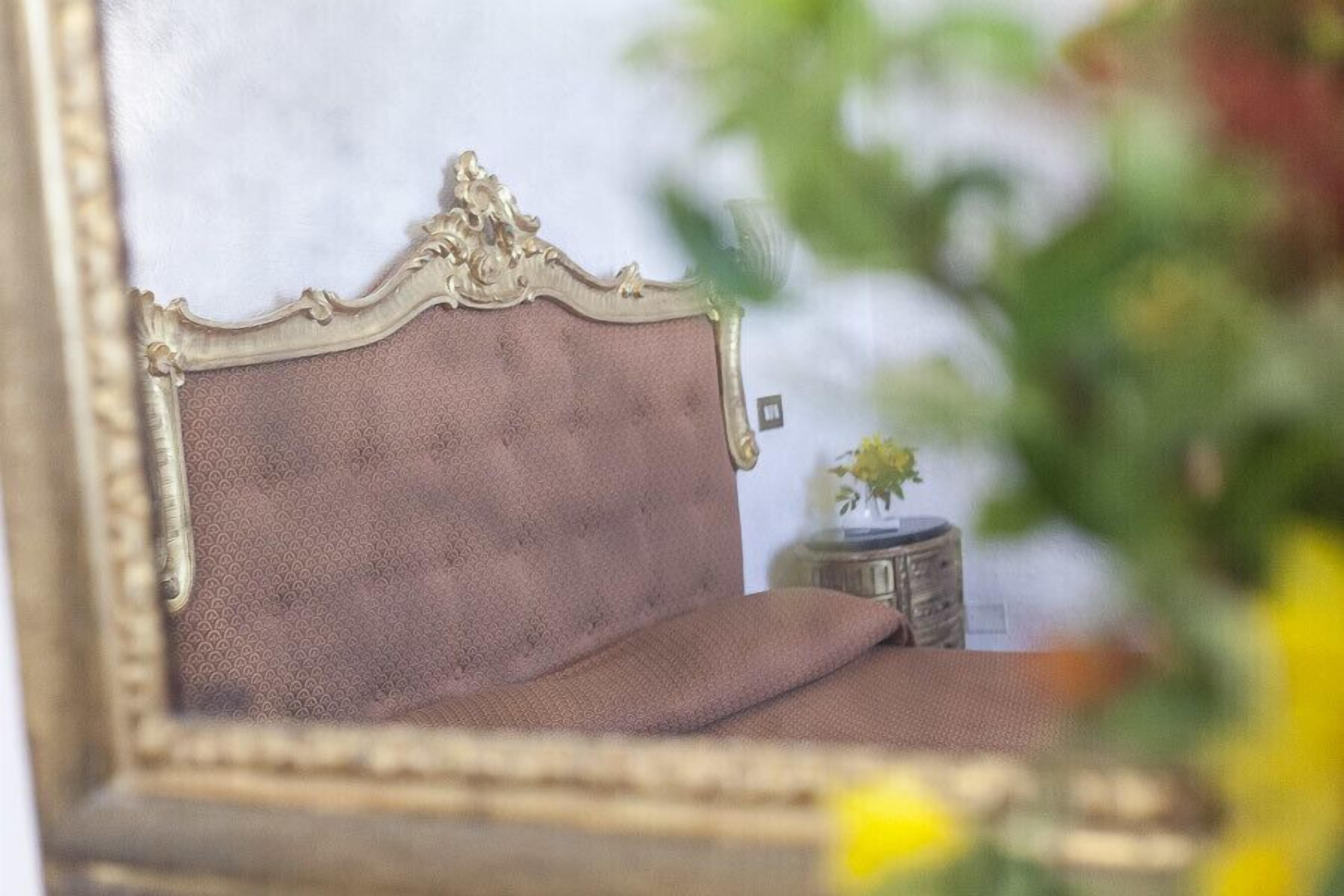 Ein bettes Stil der alten Zeit, mit Kopfteil, einem kleinen Nachttisch und einer Vase mit Blumen.