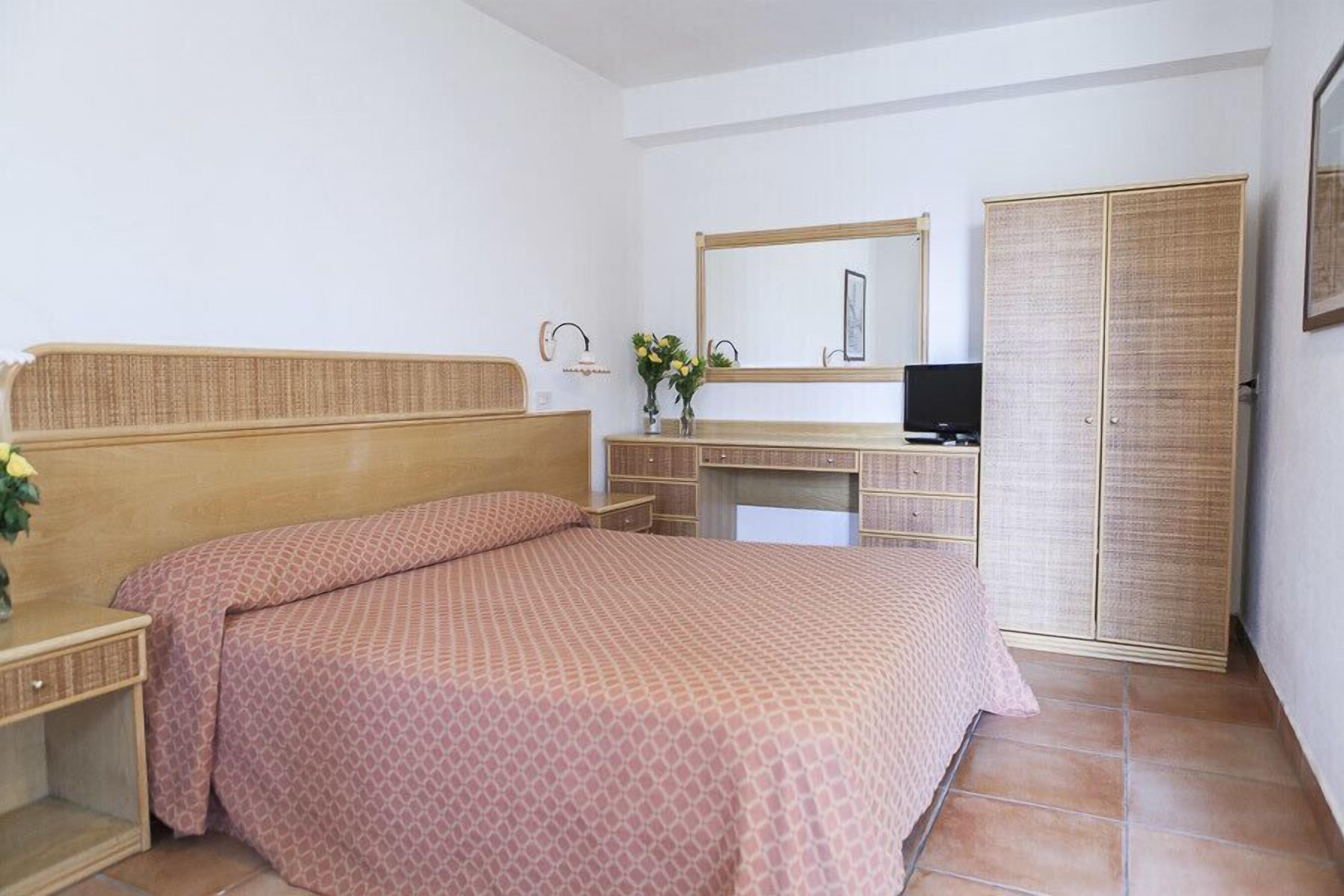 Quarto com cama, escrivaninha, televisão e guarda-roupa.