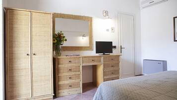 Un dormitorio con una cama, televisor, armario y escritorio con cajones.