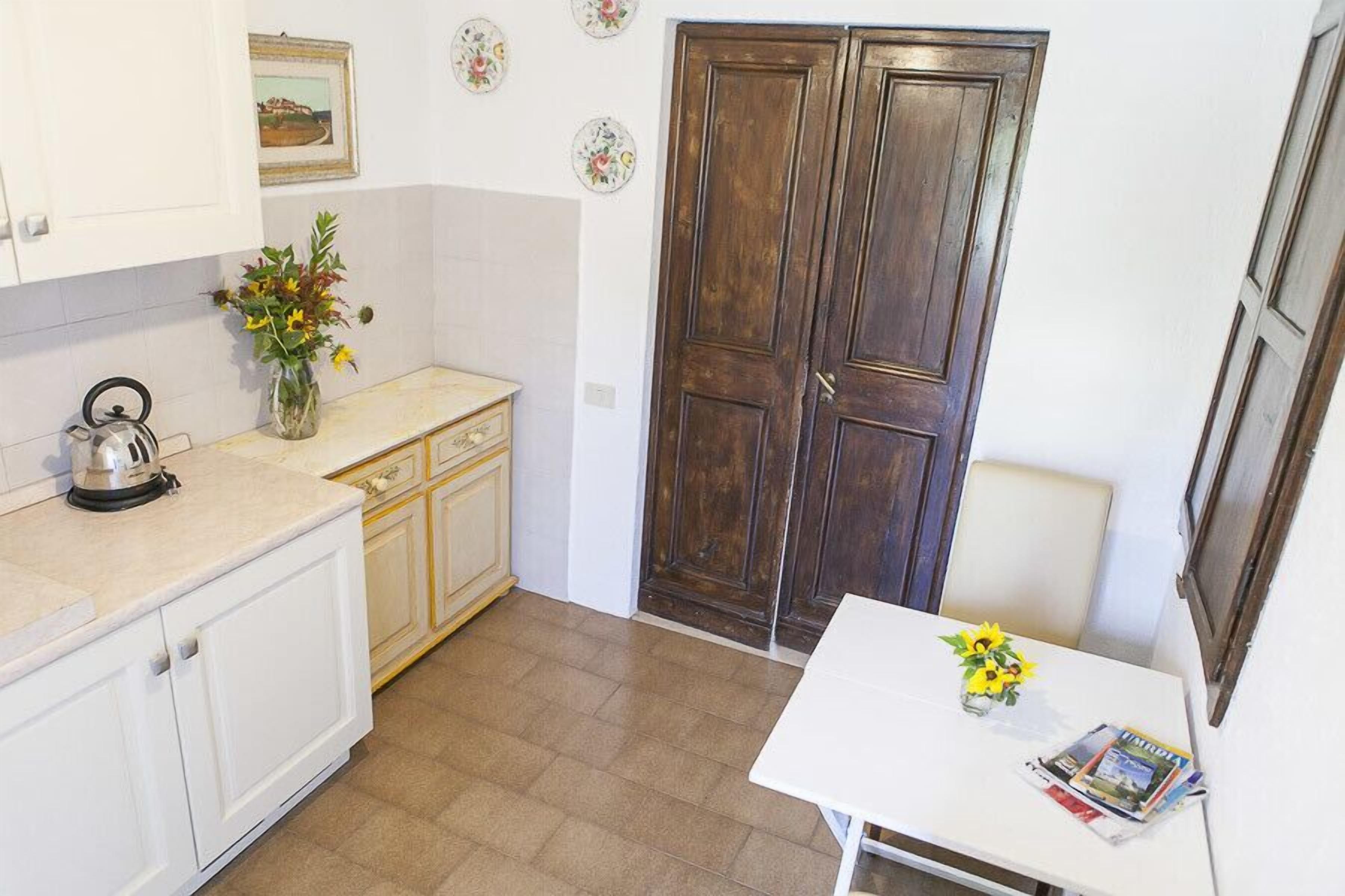 Una pequeña cocina con armarios blancos, una puerta de madera y una mesa con un jarrón de flores.