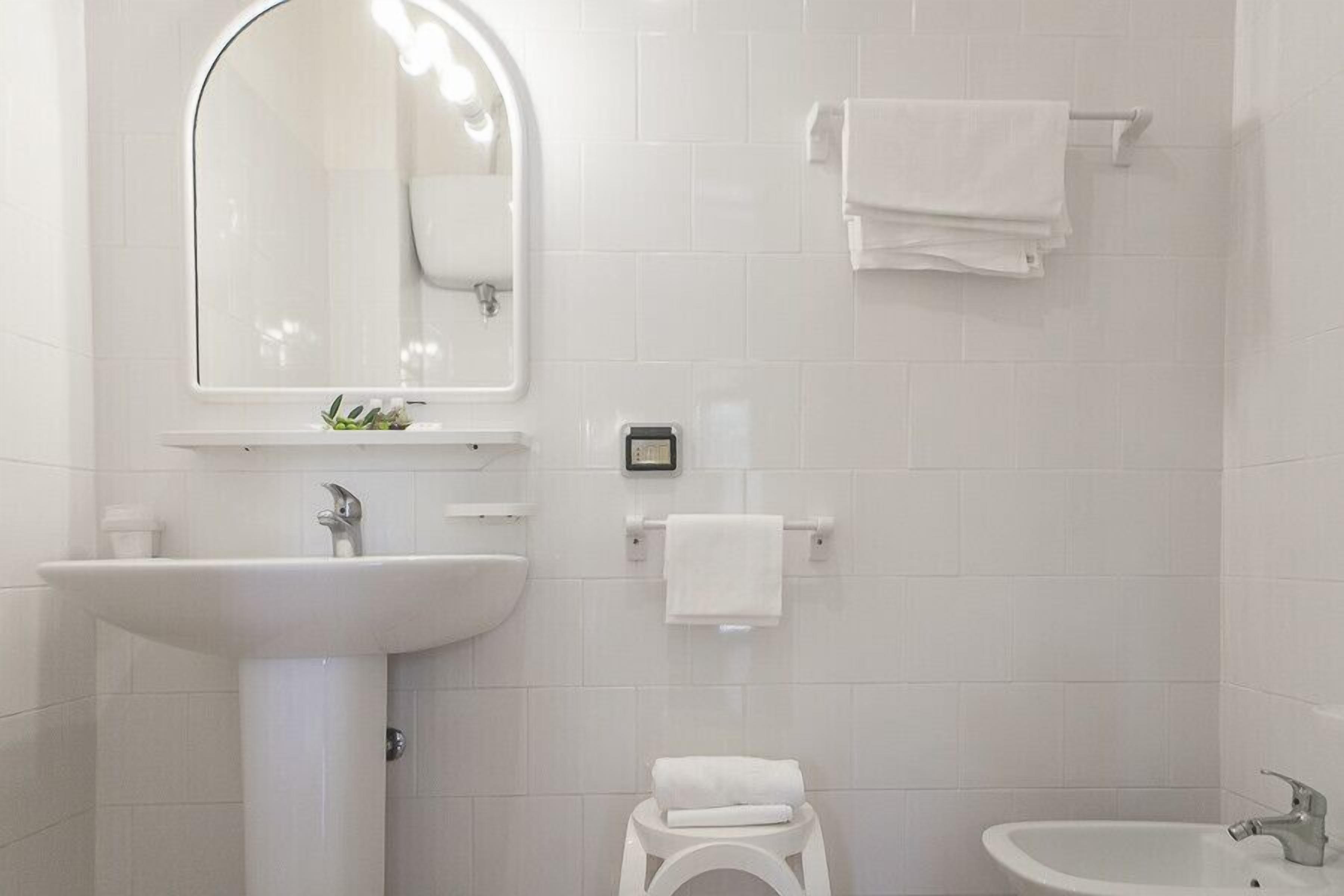 Un bagno moderno con un lavabo su piedistallo, un piccolo water, un bidet e uno specchio con illuminazione integrata.