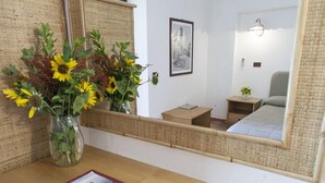 Un dormitorio con mesita de noche de madera, un espejo, un cuadro en la pared y una pequeña mesita con un florero.