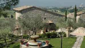 Un edificio de piedra con una fuente circular en un jardín ajardinado.