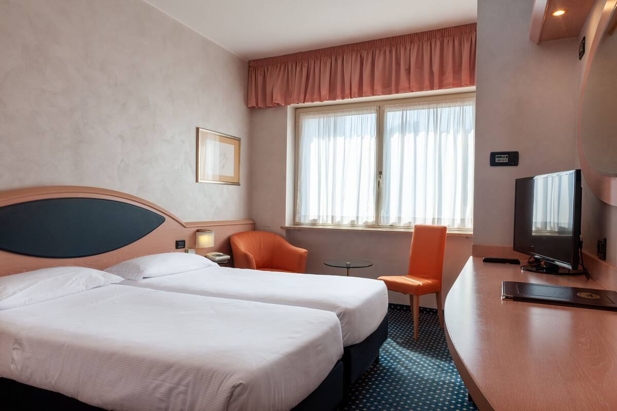 Een hotelkamer met twee bedden, een televisie, een bureau en een stoel.