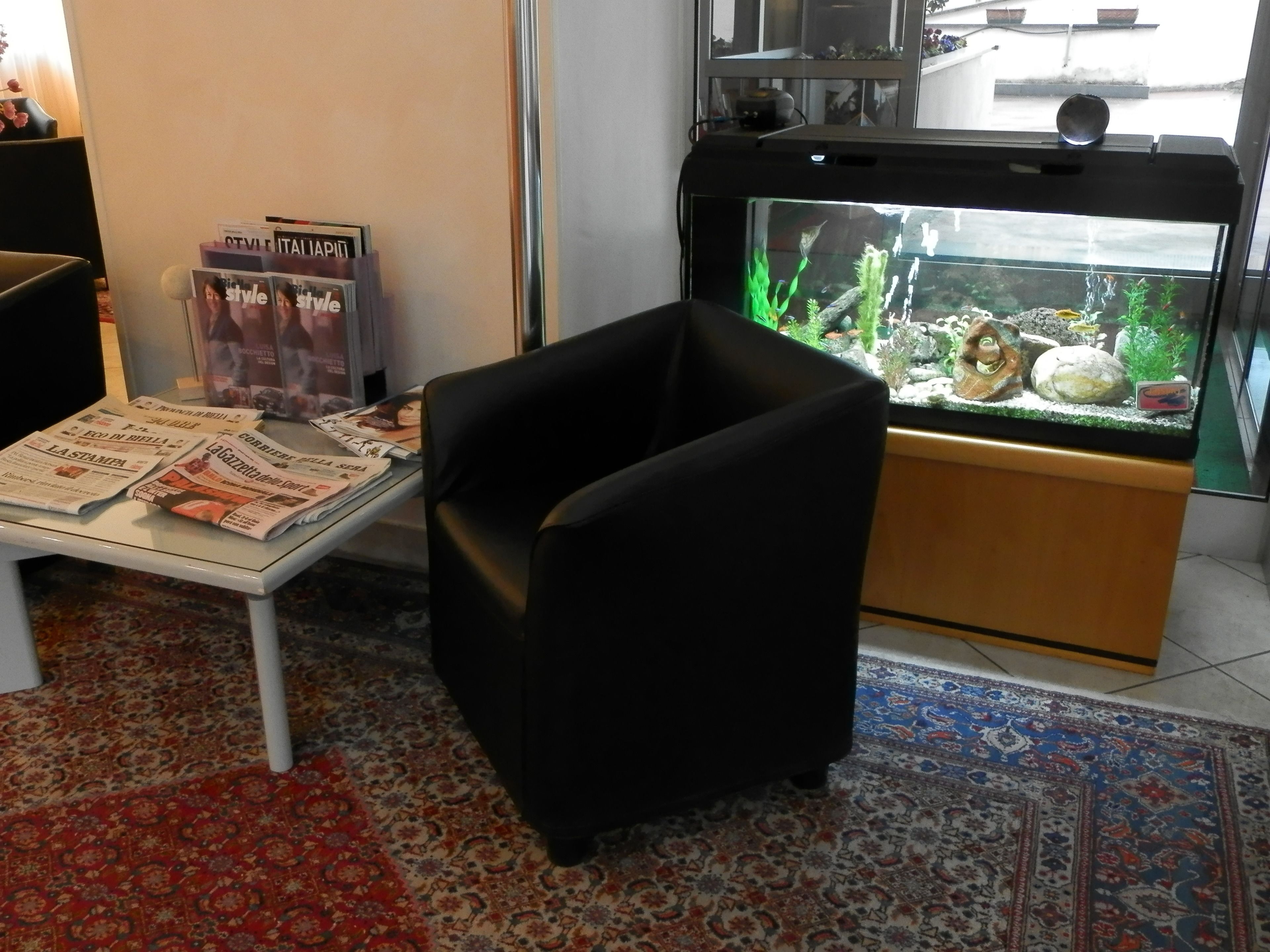 A room with a black armchair, a fish tank, and newspapers on a table.
