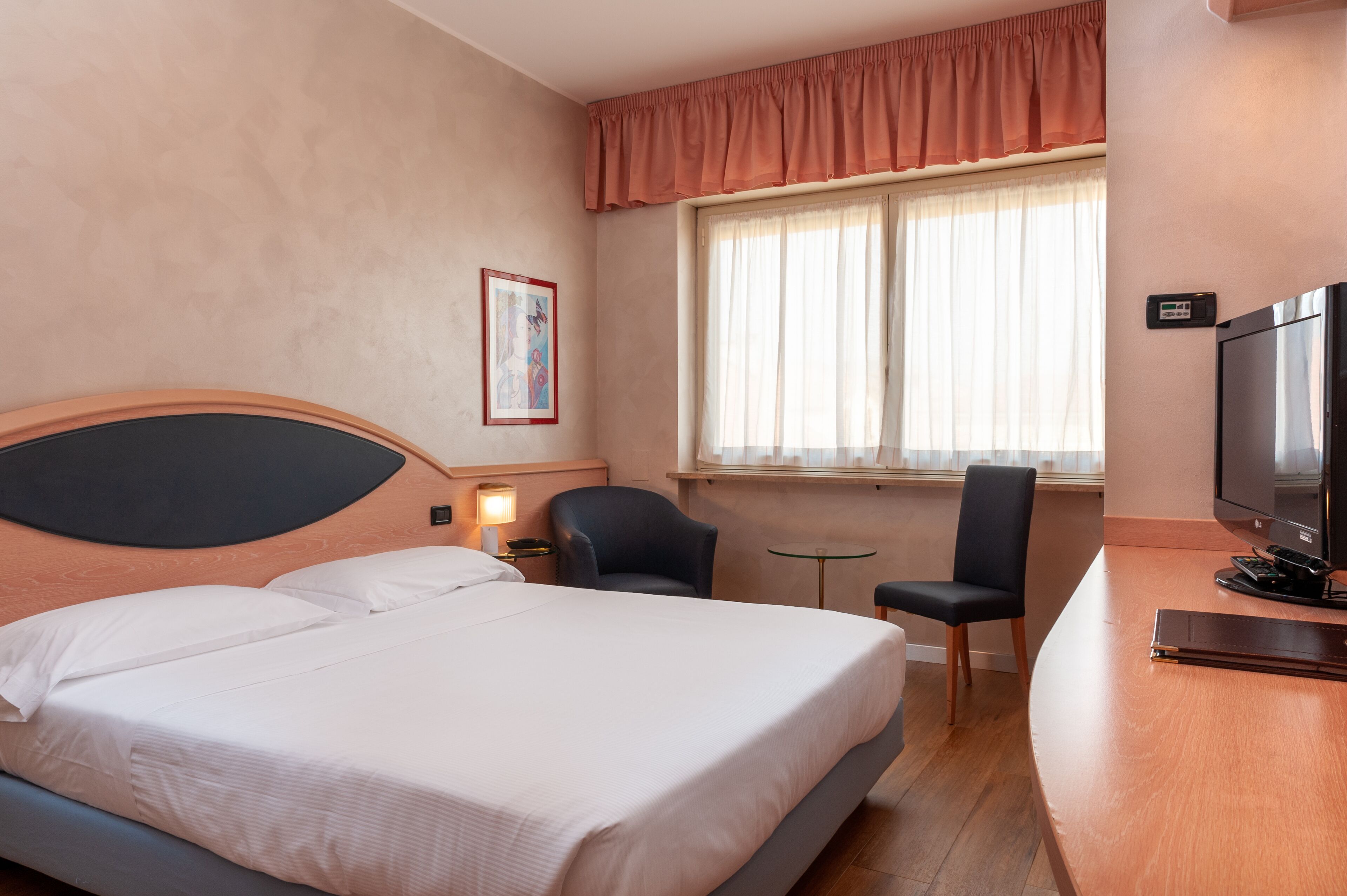 A hotel room with a bed, a desk, a chair, a television, and a window with curtains.