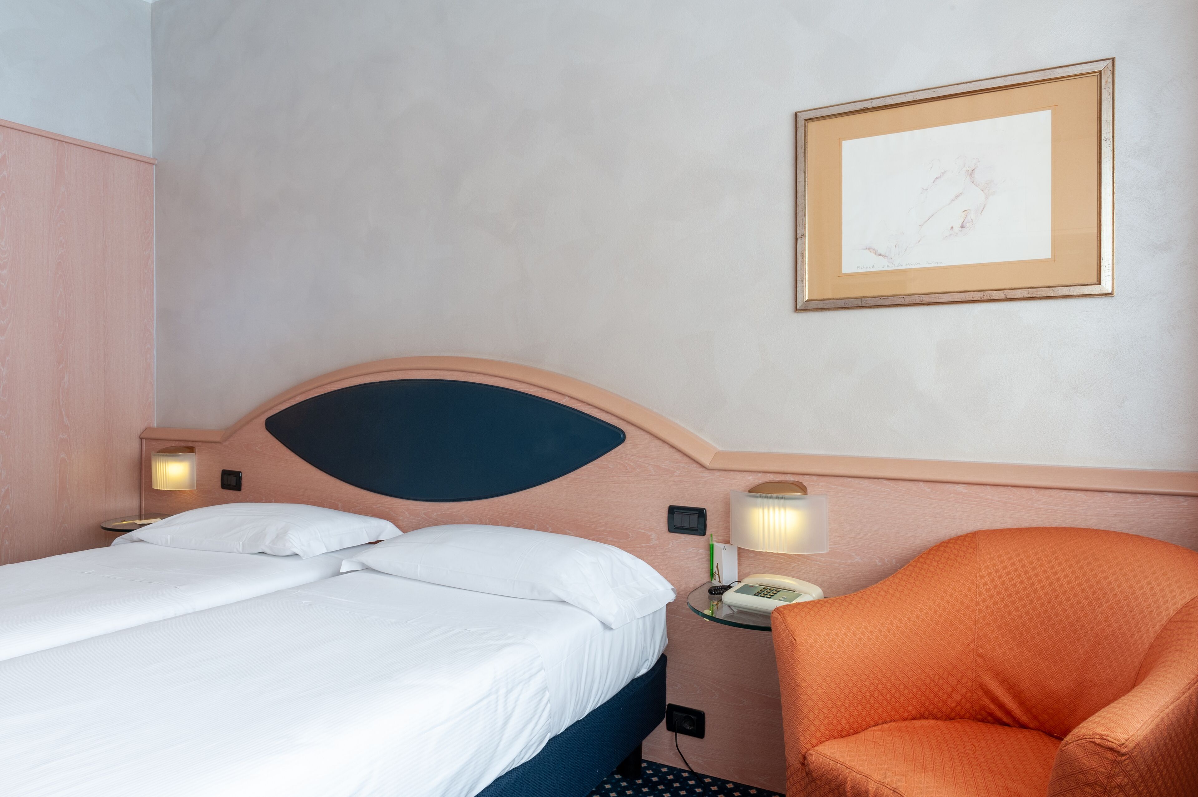 A hotel room with a bed, a chair, a bedside table with a lamp, and a framed picture on the wall.