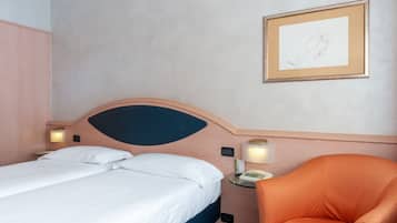 A hotel room with a bed, a chair, a bedside table with a lamp, and a framed picture on the wall.