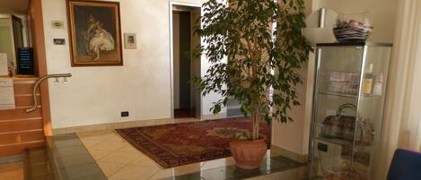 A spacious lobby with a large potted plant, a glass display cabinet with handbags, and a framed painting on the wall.