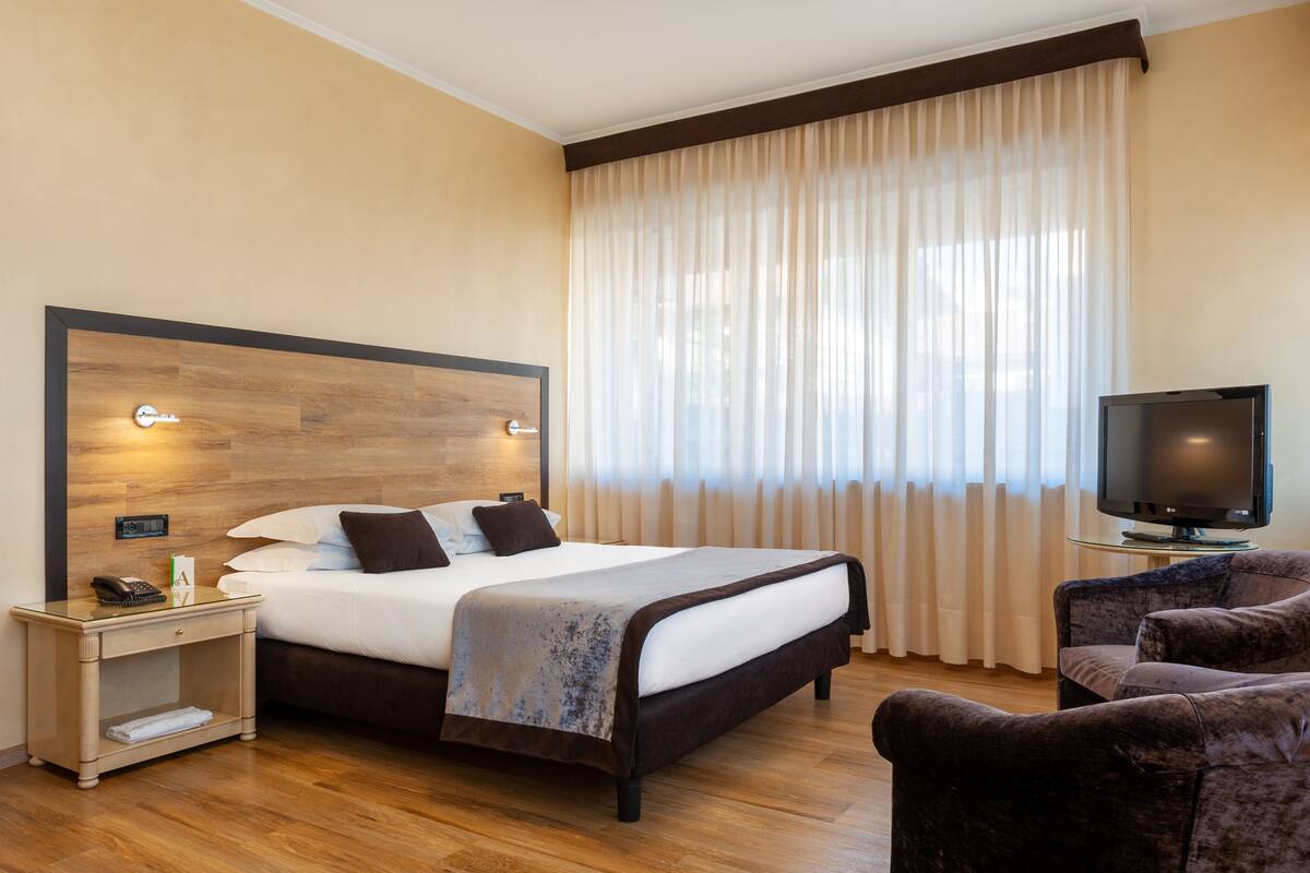 Een hotelkamer met een groot bed, een televisie, een stoel en een nachtkastje.