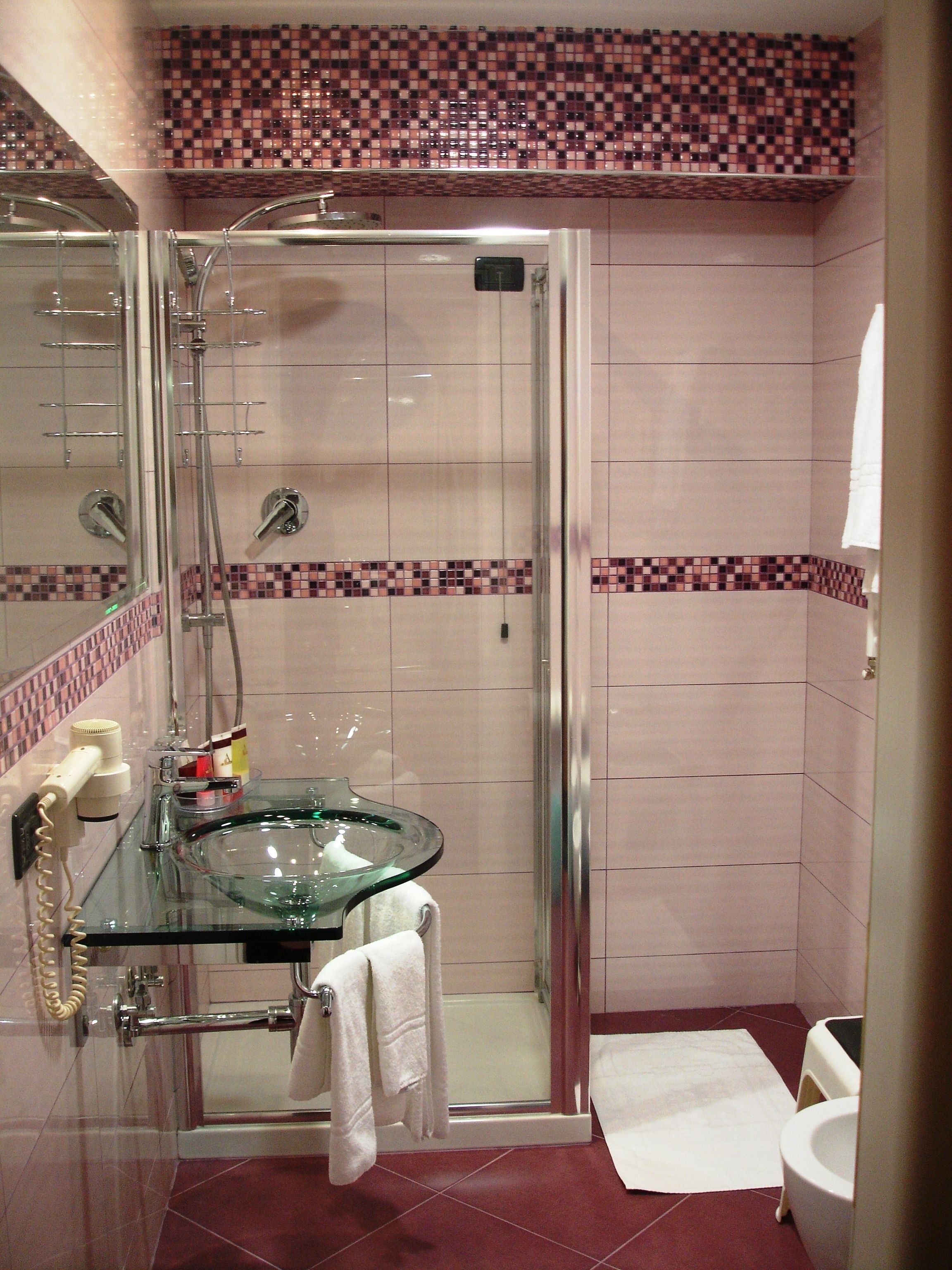 A bathroom with a glass shower enclosure, a glass sink, and a white toilet.