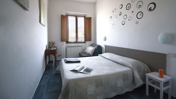 Une chambre à coucher comprenant un lit, une table de chevet, une chaise, un radiateur et une fenêtre avec des rideaux.