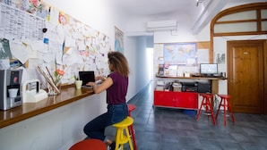 Une femme travaille à un bureau, près d’une machine à café, entourée de papiers et d’une carte accrochée au mur.