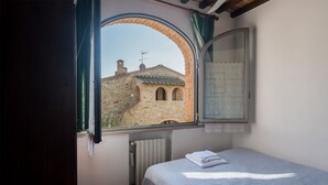 Een slaapkamer met een bed, een raam met uitzicht op een stenen gebouw en een radiator.