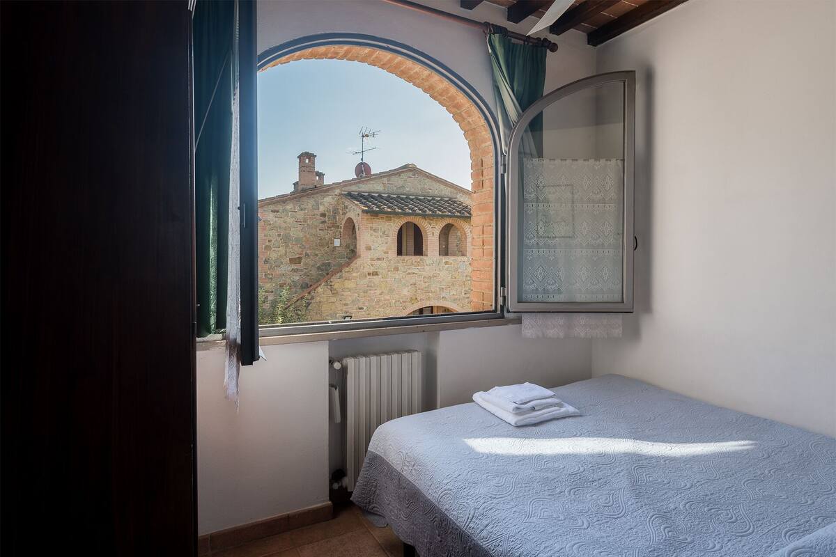 Une chambre à coucher avec un lit, une fenêtre donnant sur un bâtiment en pierre et un radiateur.