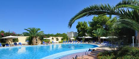 A swimming pool with blue water, surrounded by palm trees and lounge chairs.