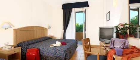 Habitación de hotel con dos camas, un escritorio con televisor, una silla, una maleta, una lámpara y una ventana con cortinas.