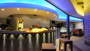 Zona de bar moderna con un mostrador curvo, taburetes y una variedad de bebidas y aperitivos.