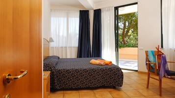A hotel room with a bed, a chair, a desk, and a window with curtains.
