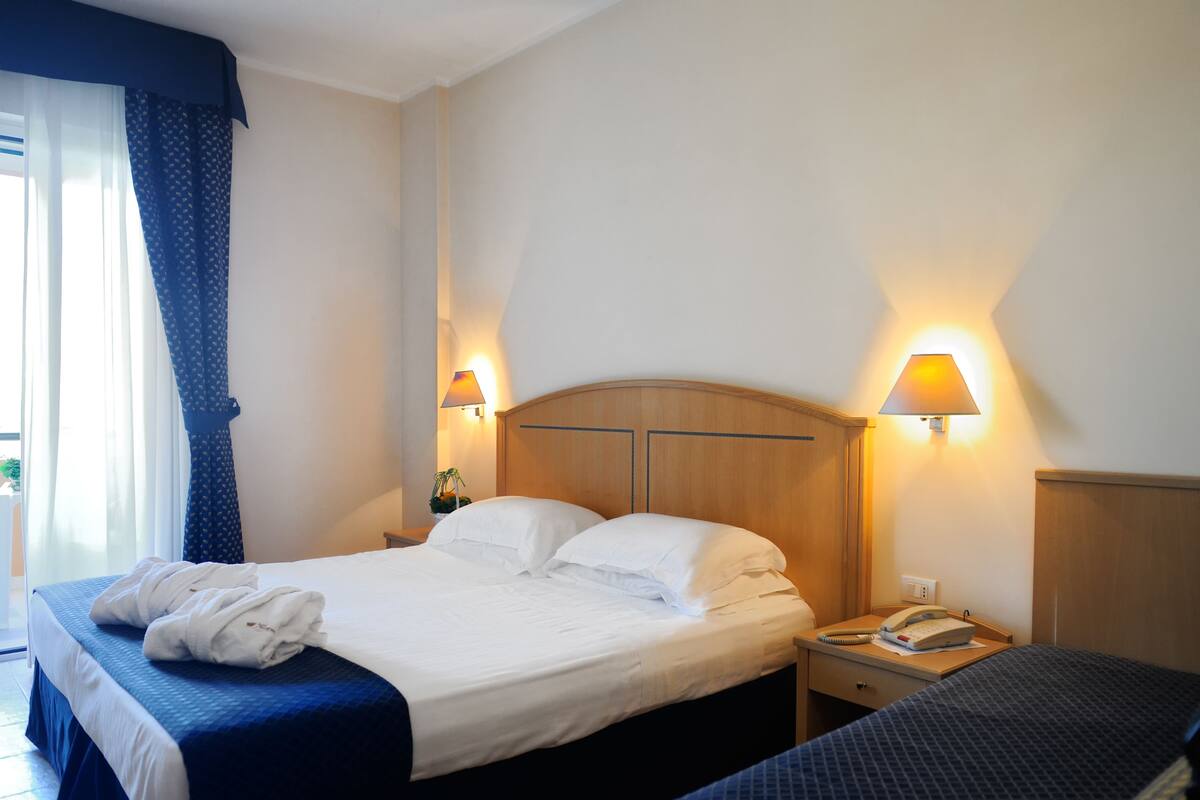 A hotel room with a bed, bedside lamps, a telephone, and a window with curtains.