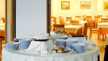 A buffet table with various pastries and stacked plates, set in a dining area with chairs and tables.